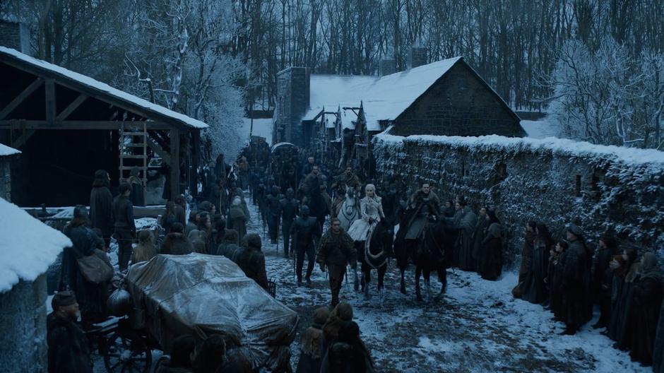 Dany and Jon ride at the front of a long line of soldiers as villages watch them pass.