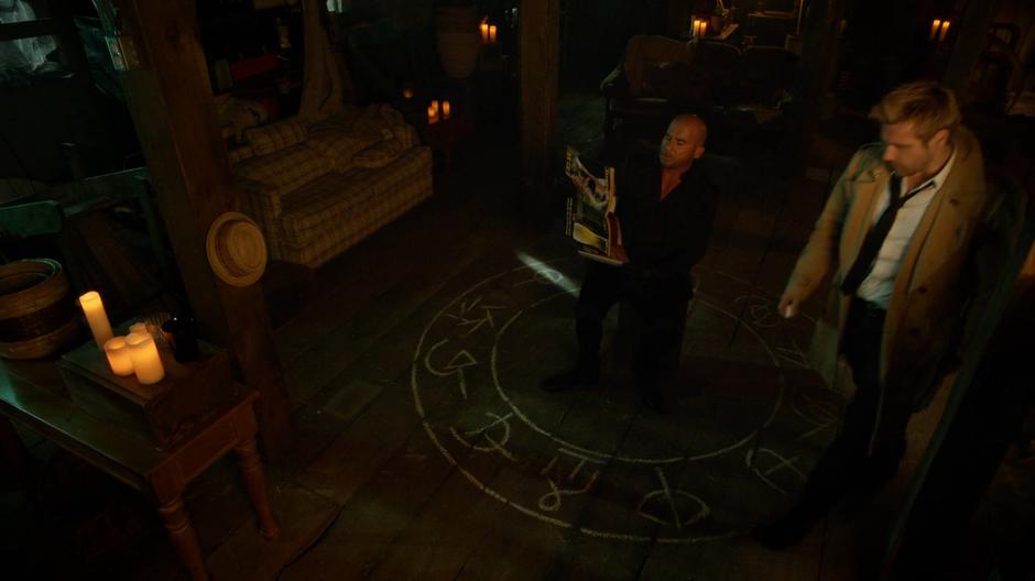 Mick reads a nudie mag while Constantine finishes drawing the protective circle.