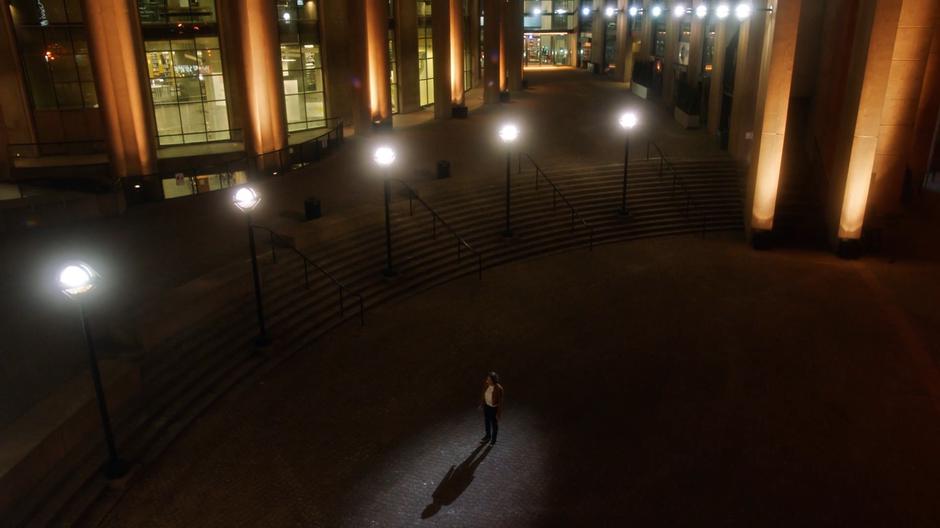 Nora stands alone in the plaza outside the bank after being left along by Barry.