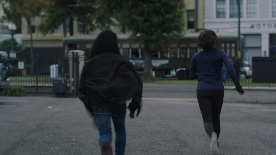 Tyrone and Adina run across a parking lot to the streetcar pulling up to the stop.