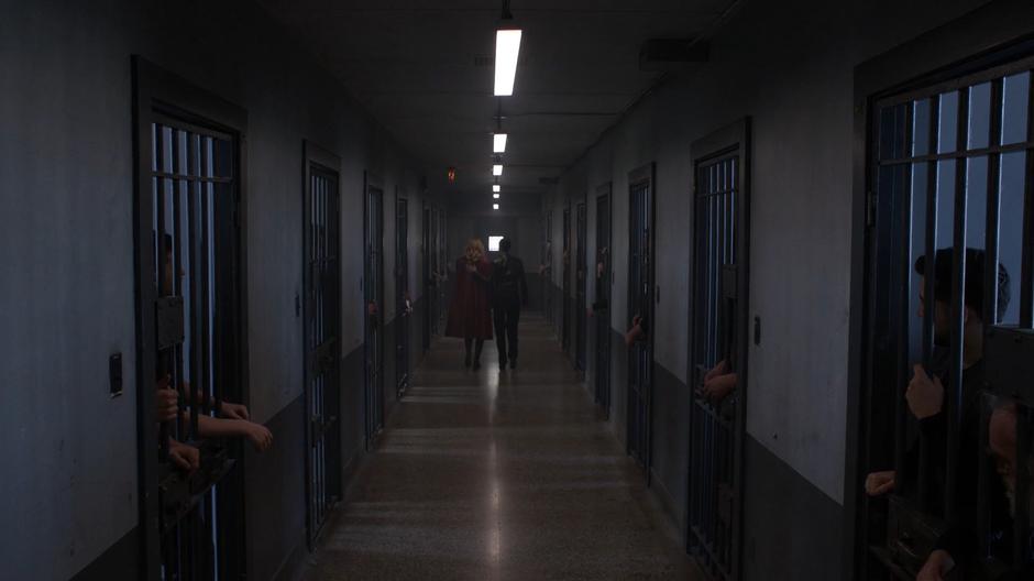 Lena puts her hand on Kara's back in support as they walk down the hallway past the inmates.