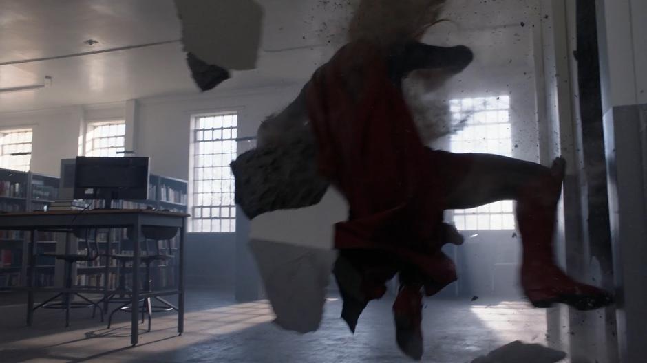 Kara is thrown through the wall into the prison library.