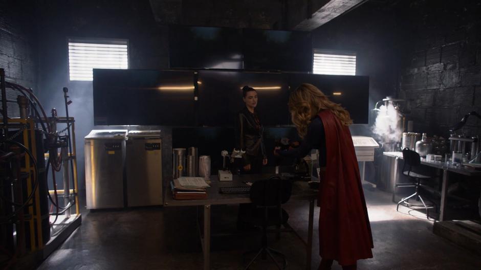 Kara examines some tech on the table in the secret lab as Lena watches her.