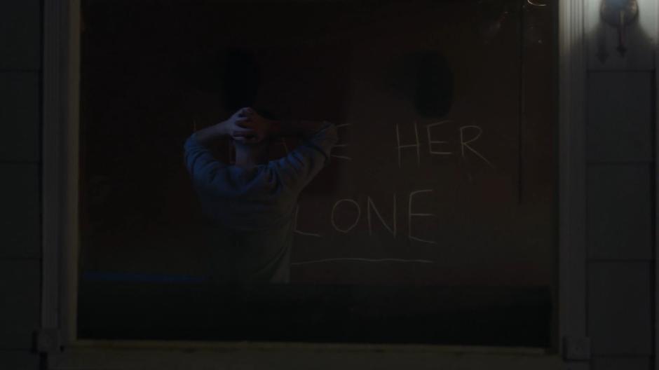 Jeremy looks at the phrase "Leave Her Alone" carved into the wall inside his house.