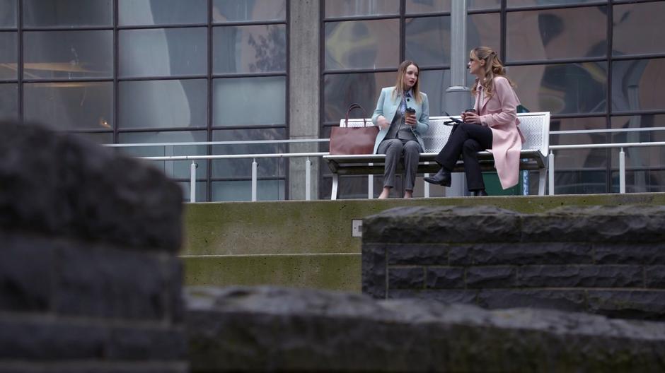 Edna tells Kara about the anti-alien sentiments spreading through the company while they sit on the bench in front of the building.
