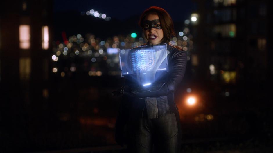 Nora examines the blueprints on her holographic display while talking to Gideon outside the building.