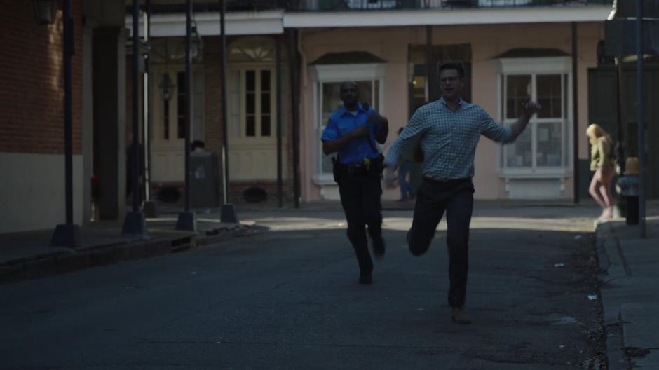 Liam runs down the street with a police officer after Tandy who is driving away.