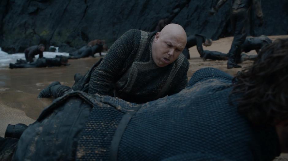 Varys drags himself ashore next to Tyrion as other survivors struggle out of the sea.