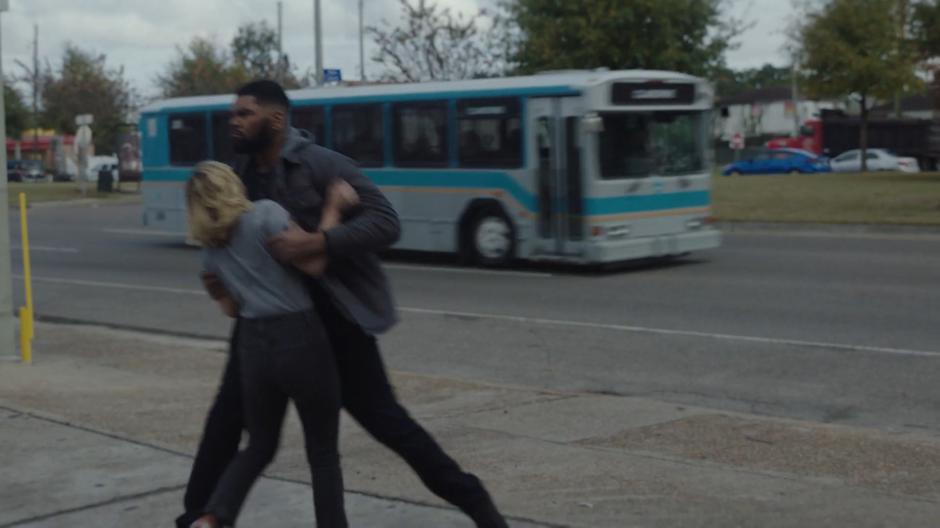 The guard grabs Tandy and pulls her back as the bus drives past just out of reach.