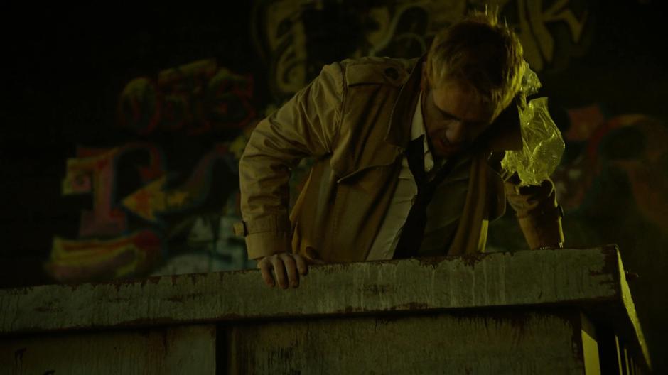 Constantine climbs out of a dumpster after landing in Hell.