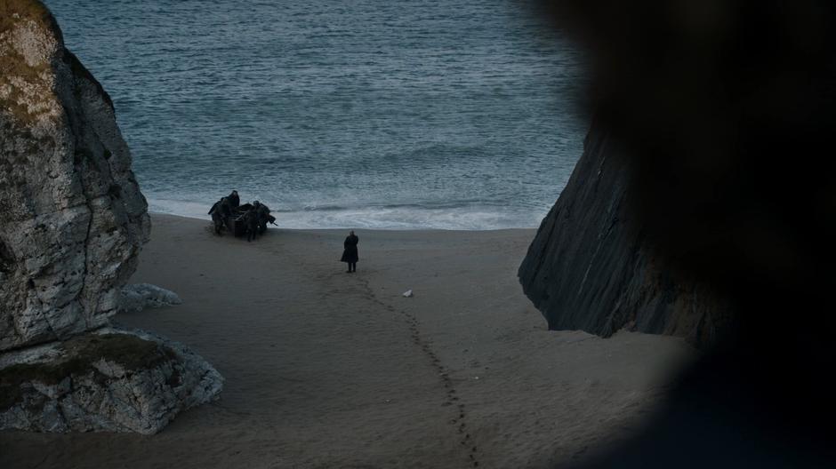Tyrone watches from above as Varys stand on the beach as Jon's boat comes ashore.