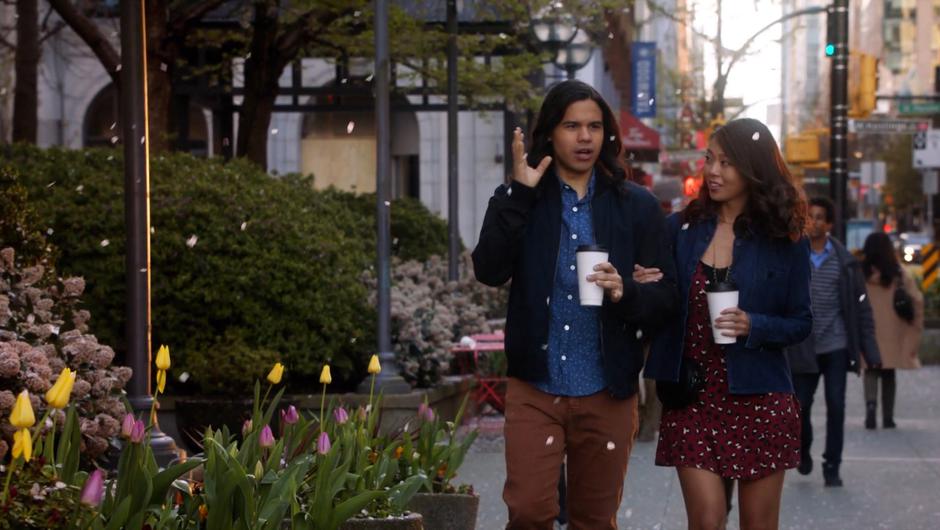 Cisco and Kamilla talk while walking arm-in-arm down the sidewalk.