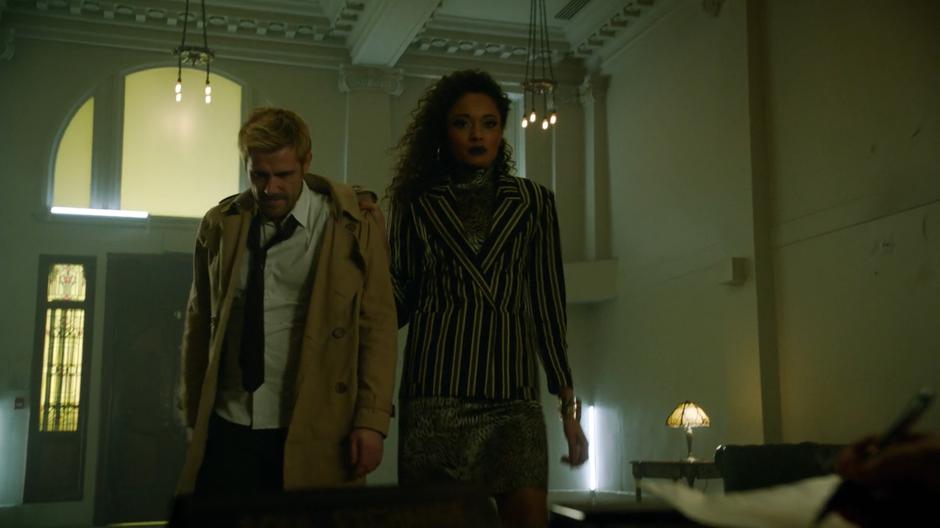 Astra drags Constantine to the teller's desk by the scruff of his coat.