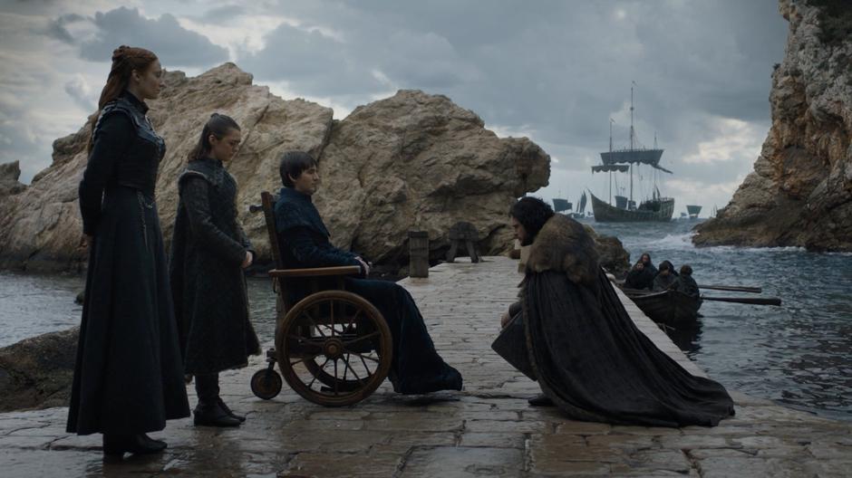 Sansa and Arya watch as Jon kneels down to say goodbye to Bran.