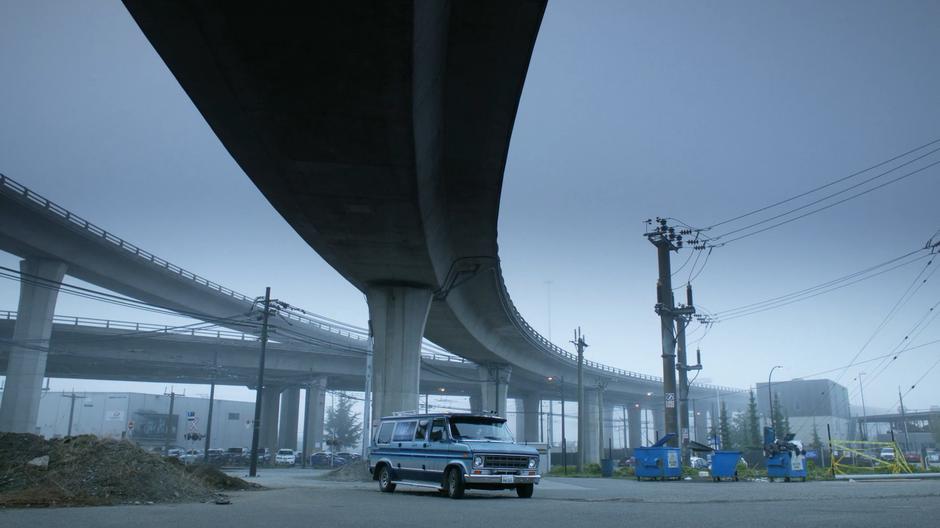 The blue kidnapping van sits under a highway bridge.