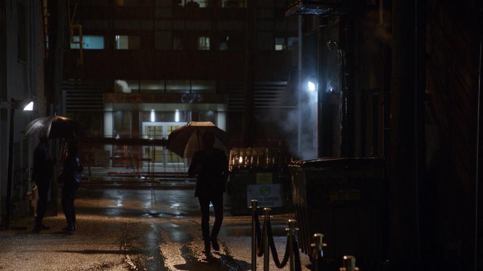 Blaine walks down the alley towards his club with an umbrella.