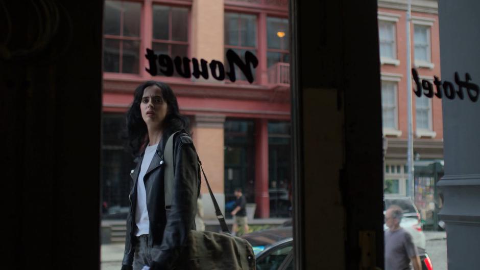 Jessica looks in through the glass door of the hotel at the rundown lobby.