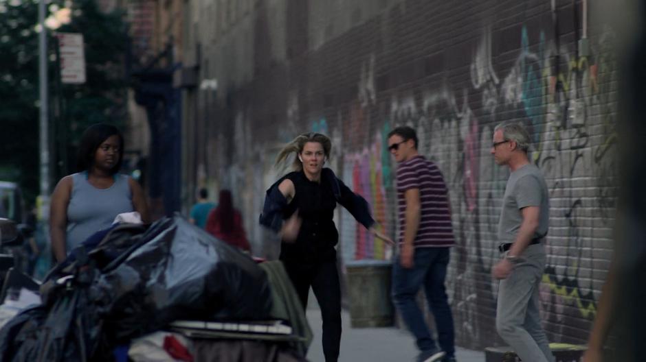 People look after Trish as she races down the sidewalk past a graffiti-covered wall.