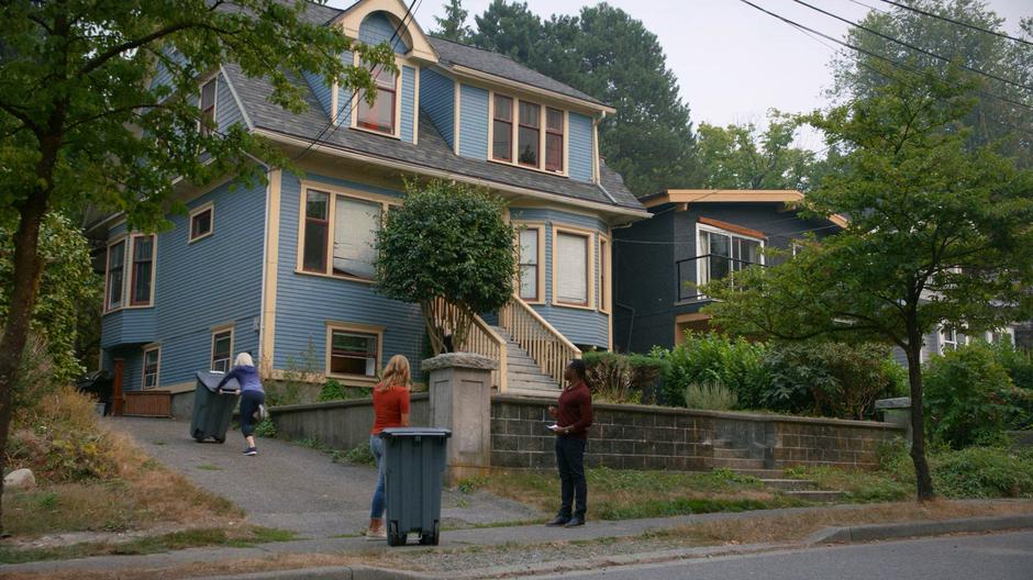 Mrs. Jones and Clive watch Liv as she runs up the driveway pushing a trash can.