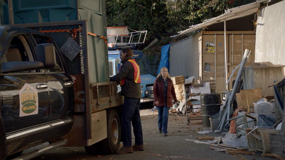 Dolly Durkins walks over as Benny secures the port-a-potty to the truck.