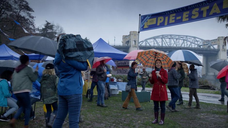 A reporter stands holding an umbrella while talking about the festival on camera.