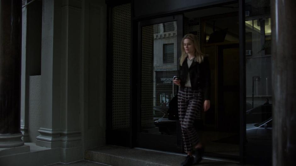 Trish walks out of the lobby of Jessica's apartment building.