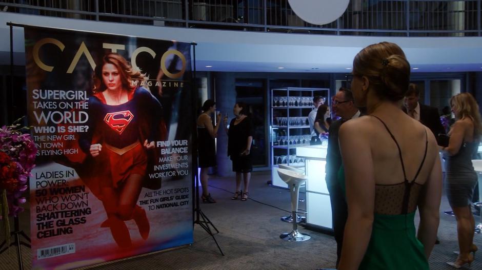 Kara looks at the giant magazine cover of herself as Supergirl.