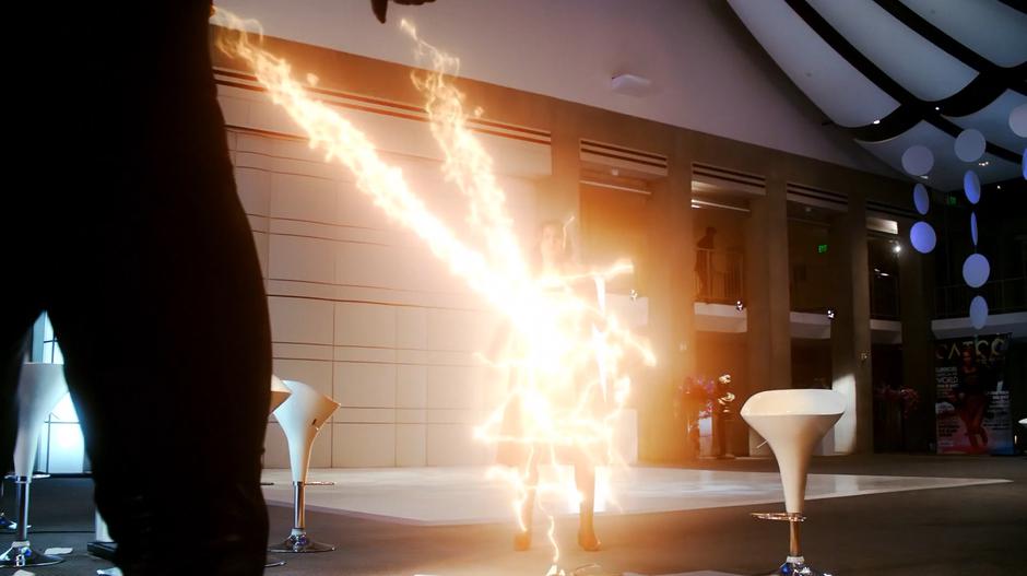 Kara blocks Reactron's energy shot to protect the attendees.