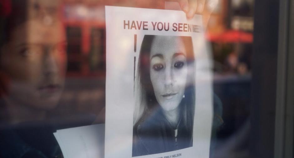 Stephanie hangs a missing person flier for Emily in the window of a shop.