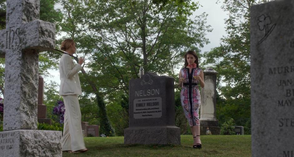 Stephanie walks around Emily's gravestone carrying two martinis to Emily.
