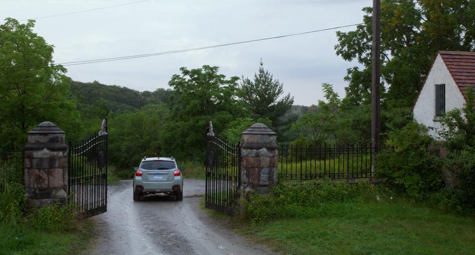 Stephanie drives through the gate though the woods towards the house.