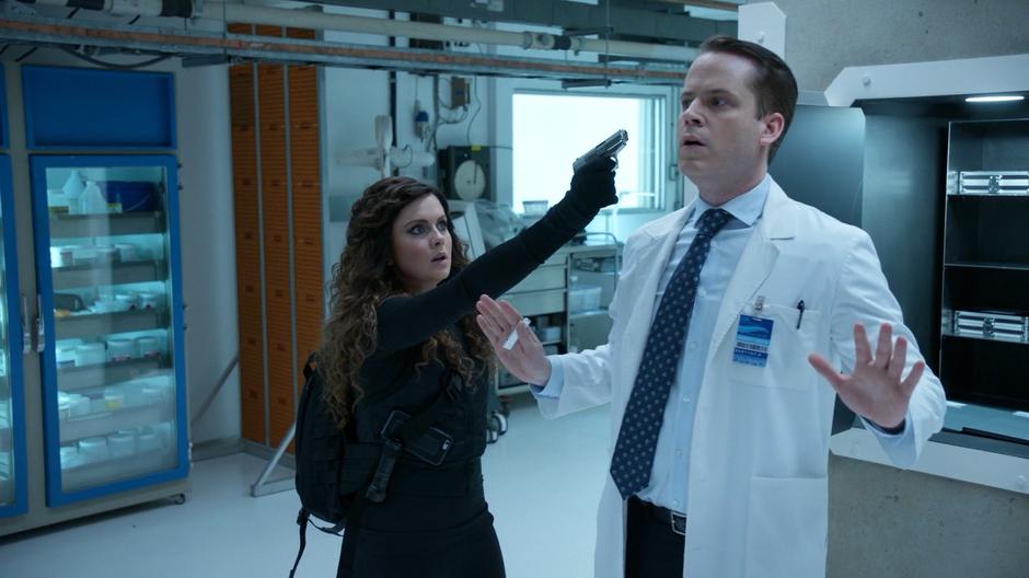Dr. Saxon puts up his hands as Liv holds a gun to his head after he has opened the vault.