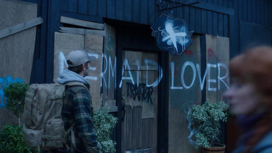 Ben looks up at the graffiti-covered boards covering the windows to the shop.