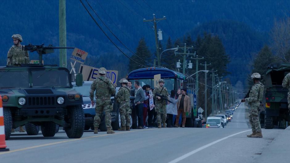 The military stops protestors from passing over the bridge as a long line of cars runs into to distance.