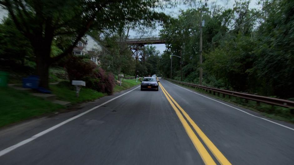 Trish and Jessica drive down the two-lane street past a train bridge into town.