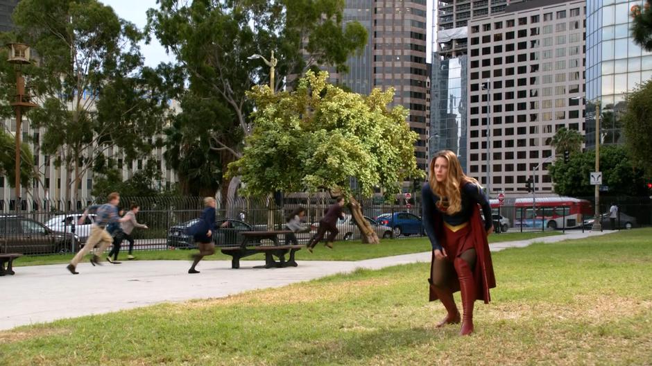 Kara lands in the park as bystanders flee behind her.
