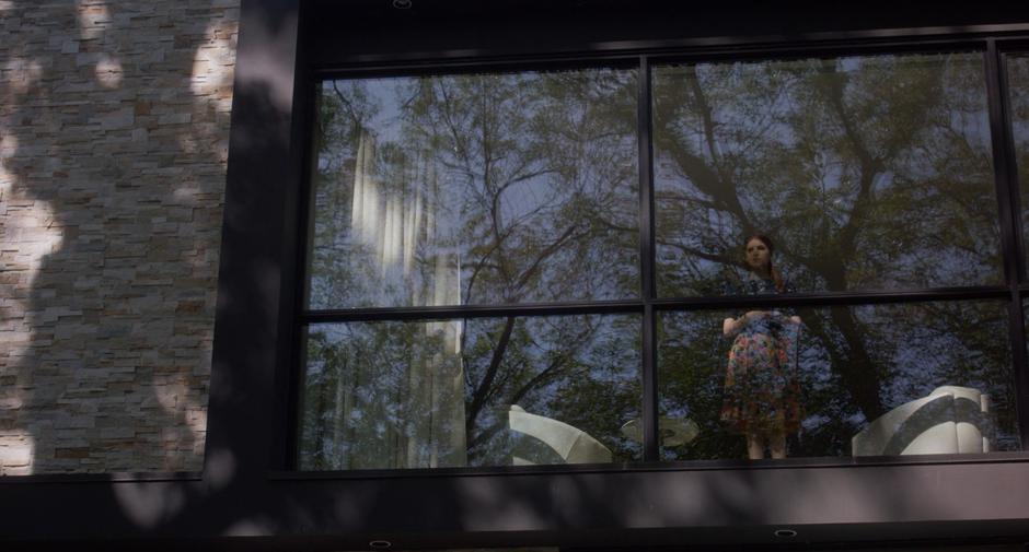 Stephanie stands at the second floor window and looks out into the back yard.