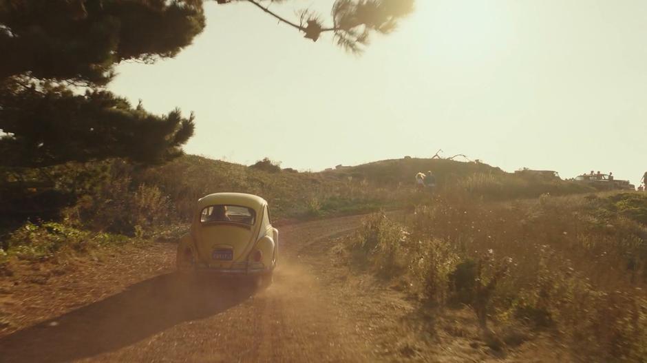 Bumblebee drives up a dirt road to where a number of cars are parked.