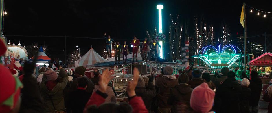 The six heroes stand on top of the fallen ferris wheel while people cheer.