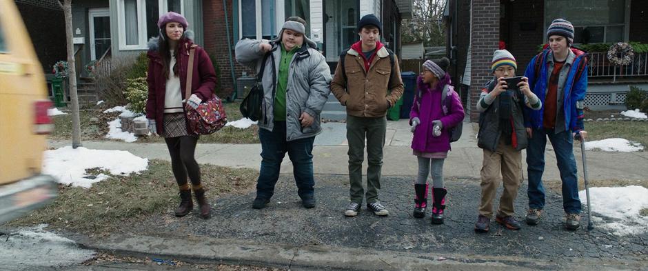 Mary, Pedro, Billy, Darla, Eugene, and Freddy stand on the sidewalk as the Vasquez van pulls away after dropping them off for school.