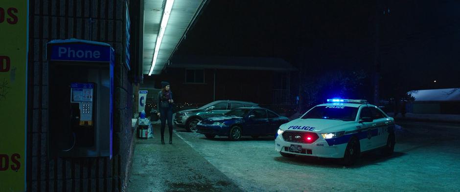 The woman approaching the store watches as a police car pulls to a stop.