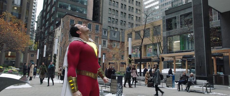 Billy stands on the sidewalk looking up at the tall building.