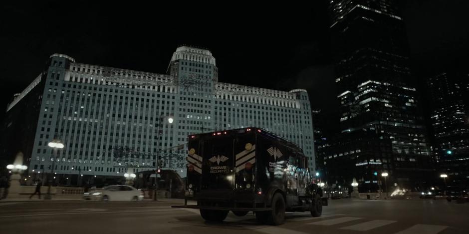 An armored Crows Security truck drives through Gotham at night.