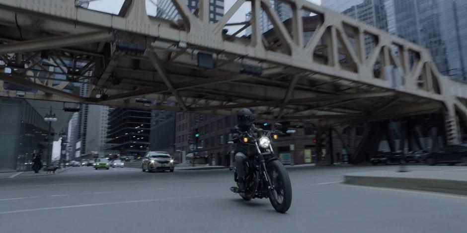 Kate rides her motorcycle under the elevated rails near the Crows Security Headquarters.