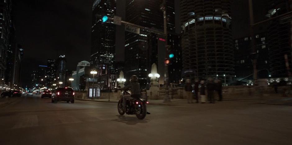 Kate rides her motorcycle across town towards Wayne Enterprises.