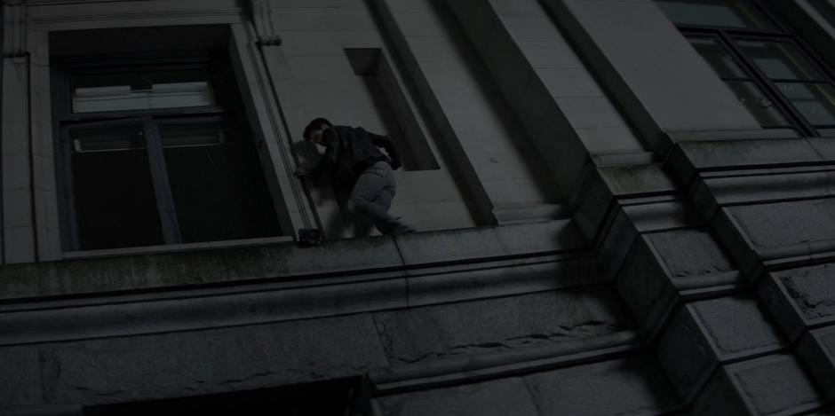 Kate carefully walks along the stone ledge to the open window.