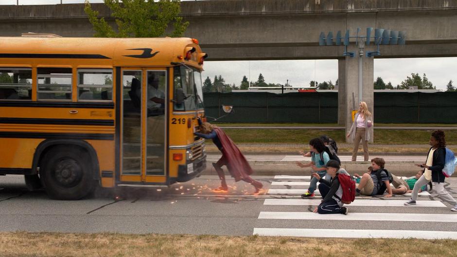 Kara's feet spark on the ground as she stops the school bus just before it hits a group of children.