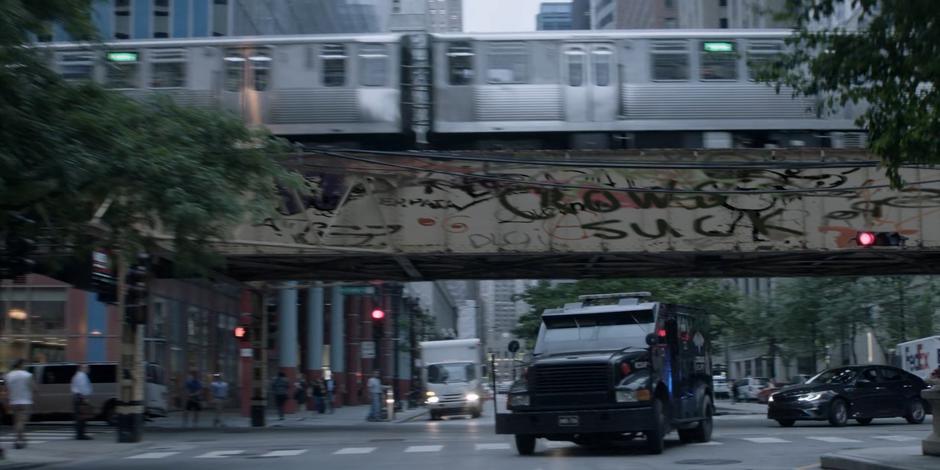 A Crows Security armored truck turns the corner as a train passes on the tracks overhead.