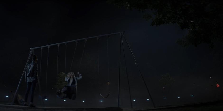 Kate stands in front of Alice who is swinging on the swing set.