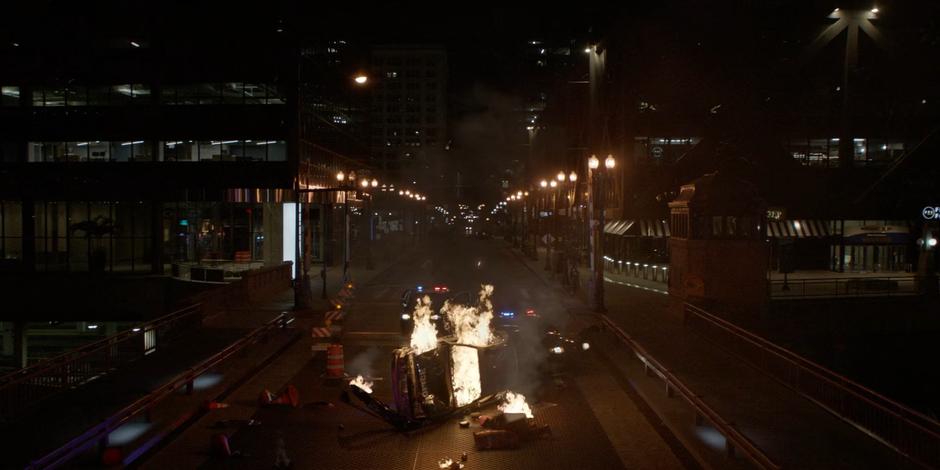 A fire engulfs an overturned police car while cops get out of the other two vehicles.